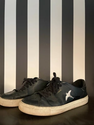 Axel arigato skor storlek 44 - Svarta låga sneakers, Axel arigato. Skorna har en vit sula och är tillverkade i läderliknande material. Perfekta för en avslappnad och trendig stil.