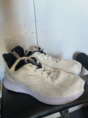 Vita sneakers med svart detalj gorilla wear - Snygga vita sneakers med svart insida och svart flik på plösen. Ovandelen är i meshmaterial för bra andningsförmåga och sulan är tjock och vit för extra komfort. Skorna har vita snören och en sportig look som passar till många stilar.