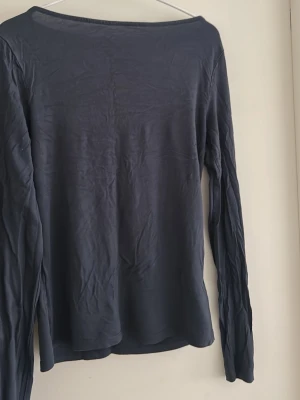 Mörkblå långärmad topp - En enkel och stilren mörkblå långärmad topp med rund halsringning. Toppen har en slim passform och är tillverkad i ett mjukt material som känns skönt mot huden. Perfekt att matcha med jeans eller kjol för en clean look.