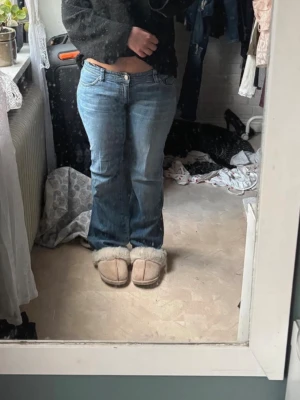 Blå bootcut jeans med detaljer - Säljer ett par blå bootcut jeans med låg midja och snygga detaljer på bakfickorna. Jeansen har klassisk femficksdesign och är tillverkade i denim. Perfekta för dig som gillar en avslappnad och trendig look. Storlek 38 men passar mer 34-36