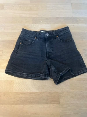 Svarta jeansshorts - Snygga svarta jeansshorts med medelhög midja och klassisk femficksdesign. Shortsen har knapp och dragkedja framtill samt raka ben. Perfekta för sommaren och lätta att matcha med olika stilar.