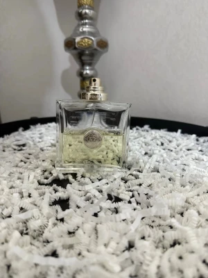 Versace Versense  - Stilren parfymflaska i genomskinligt glas med silverfärgad spraykork och rund silverdetalj på framsidan. Flaskan har en modern, fyrkantig form och innehåller en ljusgul vätska. Perfekt för dig som gillar exklusiva och minimalistiska dofter.