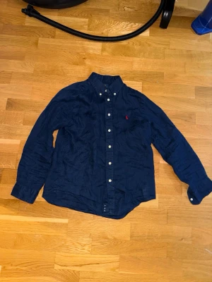 Mörkblå skjorta med knappar - Marinblå Ralph lauren linné skjorta som är i ett ganska bra skick. I princip fläckfri och är i storlek 10-12 år som motsvarar ca 150-165 cm. Ny pris är ca 1000, kom med prisförslag!