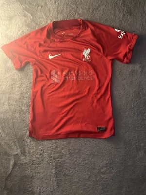 Liverpool - Snygg liverpool tröja från säsongen 22-23. Fint skick förutom en liten lös tråd på baksidan som ni ser i bild 3. Köpt helt ny för 699kr på JD utomlands. Andvänd kanske 10 gånger sen dess. Passformen är tight och stretchig, skriv till mig vid mista intresse eller småfrågor😁