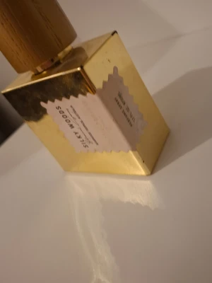 Silky Woods parfym i guldflaska - Lyxig parfymflaska i guld med trälock och etikett på framsidan där det står 'Silky Woods'. Flaskan har en fyrkantig form och ger ett exklusivt intryck. Perfekt för dig som gillar eleganta och unika dofter.nypris ca 2000