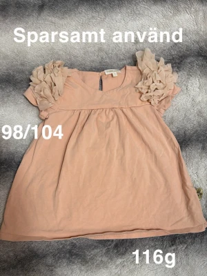 Aprikosfärgad topp med volangärmar - Supersöt aprikosfärgad topp med korta ärmar och stora volangdetaljer på axlarna. Perfekt för dig som gillar en gullig och lekfull stil.🌸 Sparsamt använd. Storlek 98/104