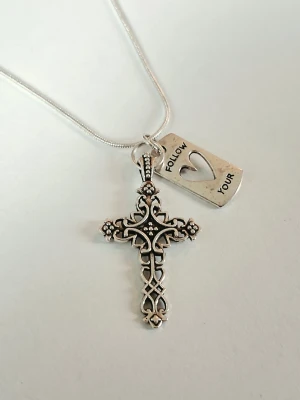 Silverhalsband med kors och textberlock - Snyggt halsband i silverfärgad metall med ett detaljerat korshänge och en rektangulär berlock med utskuret hjärta och texten 'FOLLOW YOUR'. Perfekt accessoar för dig som gillar unika smycken med budskap och vintagekänsla.