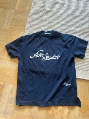 Mörkblå Acne Studios t-shirt - Snygg mörkblå t-shirt från Acne Studios med vit logga tryckt på bröstet och mindre logga vid nederkanten. Klassisk passform och rund halsringning. 