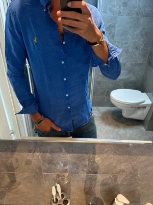 Blå linneskjorta från Ralph Lauren - Säljer en riktigt schysst linneskjorta från Ralph Lauren. Passar perfekt nu på sommaren. Jag på bilden är 188cm och bör storlek M vilket är aningen för litet. Den är i riktigt bra skick och har inga skador. Hör av er vid fler frågor:)