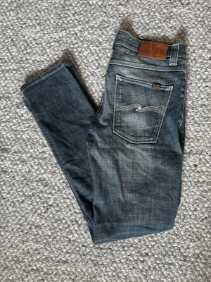 Nudie Jeans Grim tim - Säljer ett par blå slim fit jeans från Nudie Jeans med snygg slitning och klassiska kontrastsömmar. Jeansen har fem fickor, läderpatch bak och är tillverkade i denim med en cool tvättad look.