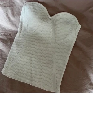 Vit ribbad bustier topp - Trendig vit bustier topp med ribbad struktur och hjärtformad urringning. Toppen är figurnära och axelbandslös, perfekt för att styla med höga jeans eller kjol. Materialet ser ut att vara stretchigt och bekvämt.