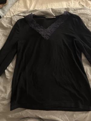 Svart långärmad topp med spets - Svart långärmad topp med v-ringning dekorerad med bred spetskant. Tunn och mjuk i materialet, perfekt för lager på lager eller som den är. Enkel men ändå elegant design som passar till mycket. Passar folk med XS/S