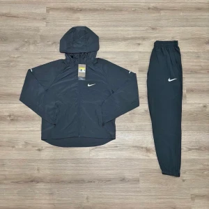 🩶Grå nike repel miller med huva🩶 - Snyggt gråt träningsset från Nike med jacka och byxor. Jackan har huva, dragkedja och vit Nike-logga på bröstet. Byxorna har resår i midjan och vid benslut samt vit Nike-logga på låret. Perfekt för träning eller chill. Överdelen är st Xs nederdelen är st S. Tar emot bud. OBS! Den är grå.