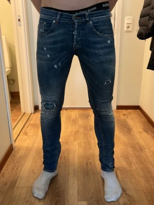 Dondup jeans - Säljer ett par blå skinny jeans med slitningar och hål på knäna. Jeansen har fem fickor, dragkedjegylf och detaljerade slitningar både fram och bak för en trendig look. Perfekta för dig som gillar en avslappnad och modern stil.