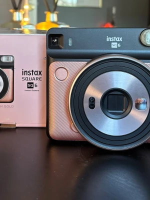 Instax SQ6 polaroidkamera roséguld - Fujifilm Instax Square SQ6 kamera i färgen roséguld (Blush Gold). Analog polaroidkamera som använder Instax Square-film i kvadratiskt format. Utrustad med inbyggd blixt, optisk sökare och frontmonterad lins. Kameran har flera exponeringslägen och inställningar som kan väljas via knappar på baksidan. Levereras med originalkartong och bruksanvisning enligt bilder.