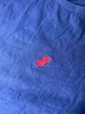 Mörkblå långärmad tröja från Polo Ralph Lauren - Mörkblå långärmad tröja från Polo Ralph Lauren med den klassiska röda broderade loggan på bröstet. Tröjan har rund halsringning och är tillverkad i mjuk bomull som känns skön mot huden. Perfekt för en clean och stilren look. Skickar alltid inom 24 timmar!