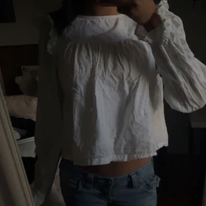 Vit blus från Gina Tricot - Söt vit blus från Gina Tricot med lång ärm och lätt rynk vid axlar och halsringning. Blusen har en luftig passform och är tillverkad i ett tunt, strukturerat tyg som ger en romantisk känsla. Perfekt att styla med jeans eller kjol.