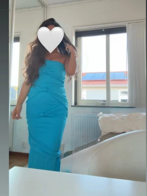 Blå axelbandslös långklänning - Snygg blå långklänning med axelbandslös design och figurnära passform. Klänningen har draperade detaljer och markerad midja för en trendig look. Perfekt för dig som vill sticka ut med en färgstark och elegant stil.