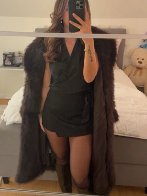 Lång mörkbrun pälsjacka - Säljer en lång och fluffig mörkbrun pälsjacka med klassisk rak passform. Jackan har bred krage och är helfodrad, perfekt för kalla dagar. Ger en lyxig och trendig look till din outfit.