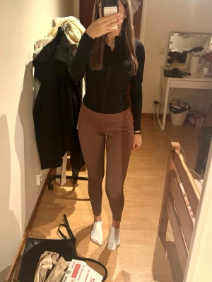 Bruna high waist leggings - Säljer ett par bruna leggings med hög midja och tight passform. De är stretchiga och sitter snyggt på kroppen, perfekta till både träning och chill. Materialet känns mjukt och följsamt. Inga synliga loggor eller märken på leggingsen.