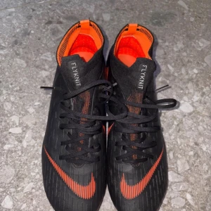 Nike Mercurial Superfly PRO Acc FG - Säljer ett par Nike Mercurial Superfly fotbollsskor i svart och orange. Skorna har hög ankel med Flyknit-material för extra stöd och en tight passform. Snygg design med orange detaljer och dobbar för spel på gräs. Perfekta för dig som vill ha speed och kontroll på planen. Skick 8/10