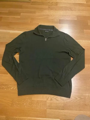 Mörkgrön halvzip från Jack & Jones - Mörkgrön stickad tröja från Jack & Jones med halv dragkedja och ståkrage. Tröjan har långa ärmar, ribbade muddar och nederkant. Perfekt för lager på lager och enkel att matcha med jeans eller chinos.
