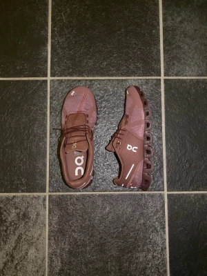  On Cloud sneakers - Snygga bruna On Cloud sneakers med vit logga och unika, dämpande sulor. Ovandelen är i mesh och textil för bra andningsförmåga. Skorna har lågt skaft och elastiska snören för enkel påtagning. Perfekta för dig som gillar sportig och modern stil. Helt nya aldrig använda. Nypris 1200. Pris kan diskuteras!