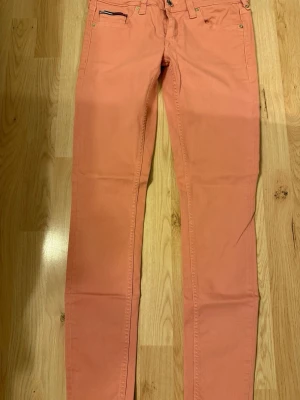 Korallfärgade skinny jeans - Säljer ett par snygga korallfärgade skinny jeans med klassisk femficksmodell och dragkedjegylf. Jeansen har smal passform och är tillverkade i ett stretchigt bomullsmaterial för extra komfort. Perfekta för dig som vill sticka ut med färg.