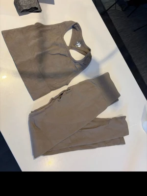 Brunt sömlöst träningsset - Säljer ett brunt sömlöst träningsset med sport-bh och höga tights. Setet är ribbat i materialet och har en tight passform som framhäver figuren. Perfekt för gymmet eller yoga. Materialet känns mjukt och stretchigt för maximal komfort.