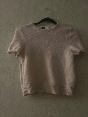 Ljusrosa stickad t-shirt från H&M - Kortärmad stickad t-shirt i ljusrosa från H&M Divided. Tröjan har rund halsringning och ribbade kanter vid ärmslut och nederkant. Perfekt för lager på lager och en avslappnad men söt look. Den är i xs men jag skulle säga att den är ganska liten i storleken. Kanin finns i hemmet