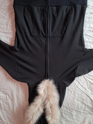 Svart hoodie med fuskpäls på huvan - Snygg svart hoodie med stor huva som har vit fuskpäls runt kanten. Hoodien har magficka framtill och är gjord i mjukt sweatshirtmaterial. Perfekt för dig som vill ha en extra cozy och trendig look.