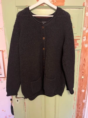 Svart stickad kofta med träknappar - Mysig svart stickad kofta med rund halsringning och träknappar framtill. Koftan har två praktiska fickor fram och långa ärmar. Storlek L. Fråga gärna om fler bilder, priset kan alltid diskuteras!