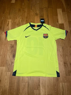 Barcelona away kit 05/06 X Ronaldinho 10 - Säljer en gul FC Barcelona matchtröja från Nike med Ronaldinho och nummer 10 på ryggen. Tröjan har klubbmärke på bröstet, mörkblå detaljer vid krage och ärmslut samt rödblå ränder på ärmarna. Perfekt för dig som älskar fotboll och klassiska spelare.