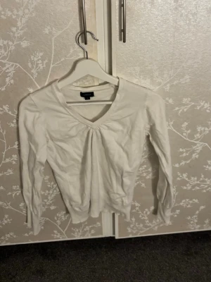 Vit v-ringad tröja från Lindex - Säljer en stilren vit tröja från Lindex med v-ringning och lätt rynkning vid halsen. Tröjan har långa ärmar och är tillverkad i ett mjukt material som passar perfekt till olika outfits.