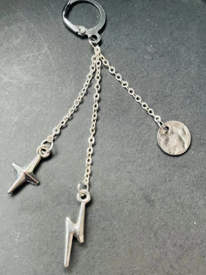 By prisförslag- 1 st Silvrigt örhänge med kedjor och berlocker - Unikt silvrigt örhänge med tre tunna kedjor, prydda med en stjärna, en blixt och en rund hamrad bricka. Snyggt statement-smycke i metall som ger en edgy och trendig vibe till din look.