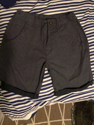 Mörkblå prickiga shorts från George - Snygga mörkblå shorts från George med små vita prickar och klassisk knappstängning. Shortsen har två sidofickor och uppvikta benslut för en avslappnad look. Perfekta för varma dagar och enkel att matcha med t-shirt eller skjorta.