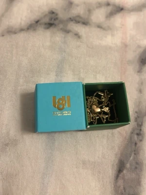 Guldhalsband med hjärthänge från Lotta hasselblad  - Snyggt guldhalsband från Lotta Hasselblad med ett litet hjärthänge. Kedjan är tunn och elegant, och hänget har en lås  detalj i mitten. Perfekt för dig som gillar stilrena smycken med en söt touch. Levereras i original ask. Väldigt fin och original pris ca 1200kr så fint och passande till mycket outfits och använd 1 gång mycket fint märke 