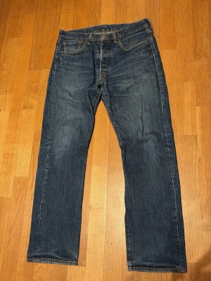 Levis jeans vintage - Säljer ett par klassiska mörkblå jeans från Levi's med rak passform och fem fickor. Jeansen har en tidlös look med subtila slitningar och är tillverkade i slitstark denim. Perfekta för dig som gillar en enkel och clean stil