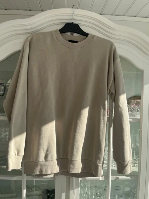 Beige sweatshirt från SMOG - Säljer en beige sweatshirt från SMOG i relaxed fit. Tröjan har rund halsringning, ribbade muddar vid ärmslut och nederkant samt är tillverkad i mjukt bomullsmaterial. Perfekt för en chill och enkel stil.