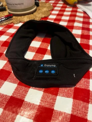 Svart trådlöst pannband med hörlurar - Säljer ett svart pannband med inbyggda trådlösa hörlurar från Enjoying. Perfekt för träning eller när du vill lyssna på musik utan vanliga hörlurar. Mjukt tyg och smidig kontrollpanel med knappar för volym och play/pause.