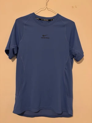Blå Nike Pro Dri-FIT träningströja - Snygg blå träningströja från Nike Pro med Dri-FIT-teknologi som håller dig torr under träningen. T-shirten har korta ärmar, rund halsringning och diskret Nike Pro-logga på bröstet. Perfekt för gymmet eller löprundan.