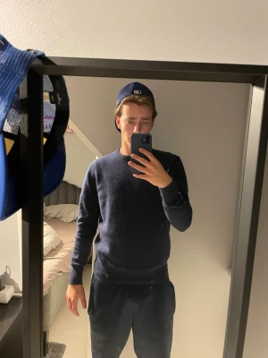 Mörkblå stickad tröja från carmés - Mörkblå stickad tröja med rund hals och långa ärmar. Tröjan har en klassisk, rak passform och är tillverkad i ett mjukt material som passar perfekt till vardagslooken. Passar S och är från Carmés