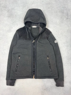 Mörkgrå hoodie från Moncler - Snygg mörkgrå hoodie/cardigan från moncler med lite päls material på axlarna. Perfekt nu inför kommande vår/sommar. Storleken är L men sitter lite mindre (M/L) . Hör av er om funderingar eller frågor.