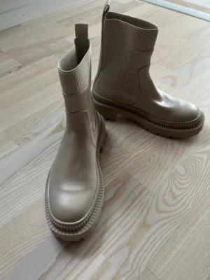 Beige  stövletter från Mango, 35 - Ny beige stövletter från Mango med grov sula och ribbade skaft i stretchigt material. Snygg minimalistisk design i syntetmaterial som ger en modern look. Perfekta för dig som gillar trendiga boots med högt skaft och coola detaljer.