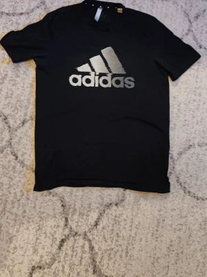 Svart Adidas t-shirt med fadead vit logga - Snygg svart t-shirt från Adidas med stor vit logga på bröstet och mindre logga i nacken. Klassisk passform och rund halsringning. Perfekt för dig som gillar sportig stil och vill ha en enkel men stilren look. Storlek small och är i toppskick. Pris är ej hugget i sten.