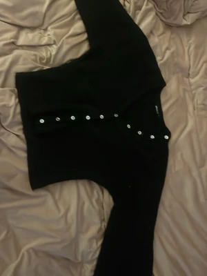 Svart kofta från Gina Tricot - Snygg svart kofta från Gina Tricot med v-ringning och silvriga knappar framtill. Koftan har lång ärm och är stickad i mjukt material, perfekt att slänga över en topp. Enkel och stilren design som passar till det mesta. Har använt typ två gånger så den är väldigt ny och den är väldigt fin o passar till typ allt.