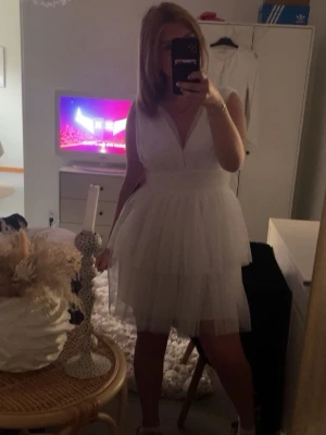 Vit kort tyllklänning med v-ringning - Säljer en vit kort klänning med flera lager tyll och djup v-ringning. Klänningen har ärmlös design och markerad midja som ger en feminin siluett. Perfekt för sommarens alla tillfällen! 💫