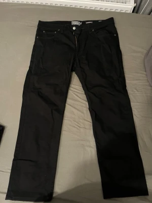 Svarta raka jeans från Jack & Jones - Snygga svarta jeans från Dressman  med rak passform och klassisk femficksdesign. Jeansen har knappgylf och är tillverkade i ett mjukt bomullsmaterial med lite stretch för extra komfort. Perfekta till en avslappnad stil.