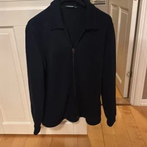 Marin blå zip overshirt. Original pris 2450 kr - Snygg marinblå jacka från J. Lindeberg med dragkedja framtill. Perfekt för en stilren look. Jackan har en klassisk krage och är tillverkad i bomull.