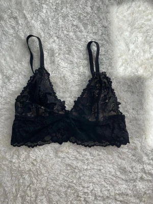 Svart spets bralette - Säljer en snygg svart bralette med spetsdetaljer och tunna axelband. Den har triangelformade kupor och är tillverkad i ett mjukt spetsmaterial som ger en romantisk look. Perfekt för dig som gillar stilrena och bekväma underkläder.